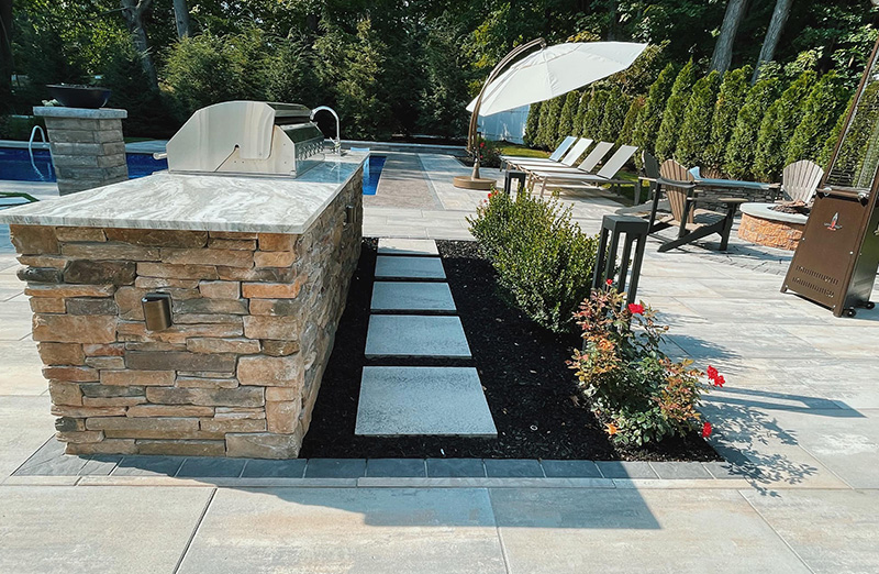 Outdoor kitchen on a paver patio by a swimming pool installed by BlackDiamondDesign Landscaping